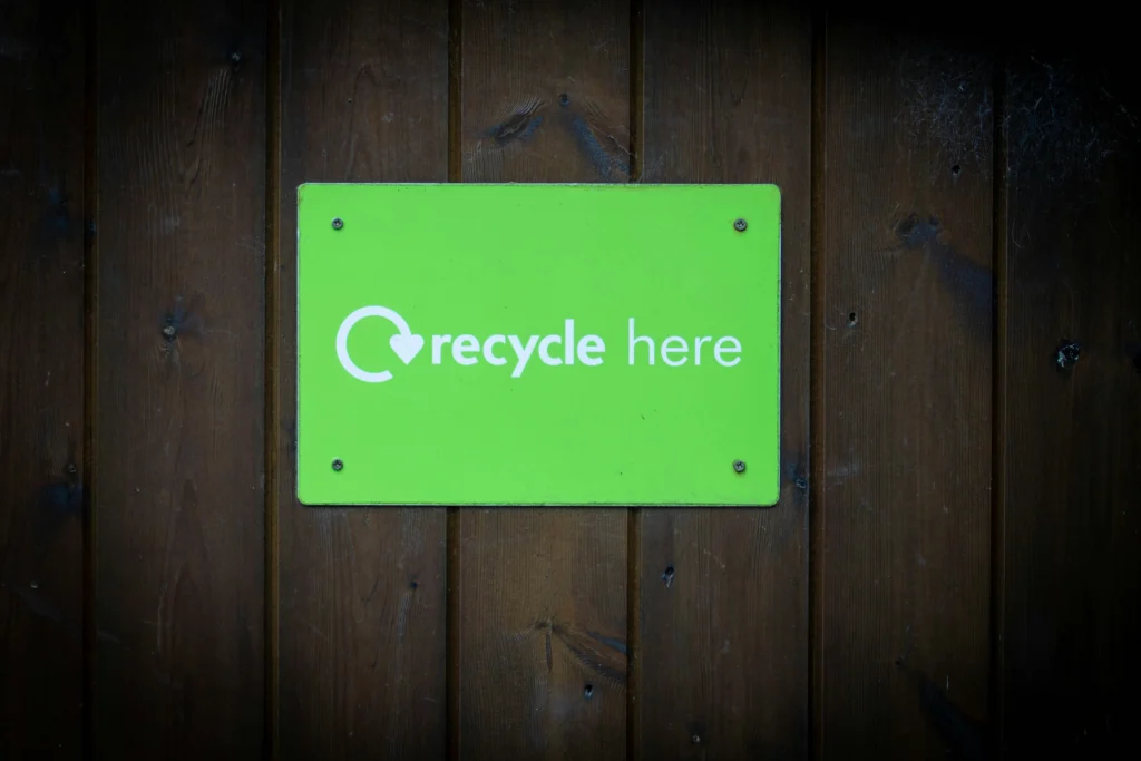 Pancarte verte accrochée sur une porte en bois sur laquelle est inscrit en anglais "Recycle here" avec une flèche. Cette inscription "Recycler ici" indique aux collaborateurs où ils faut recycler avec de bien informer et de sensibiliser chaque acteur interne à les gestions des déchets en entreprise